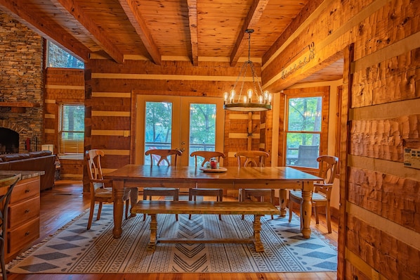 A wooden cabin interior with a dining table, chairs, and a chandelier.