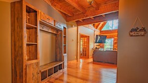 A wooden interior with a built-in TV shelf, a welcome sign, and a kitchen area with a window. - Burnt Mountain Waterfront Log Cabin, with 6person Spa  (Big Canoe)