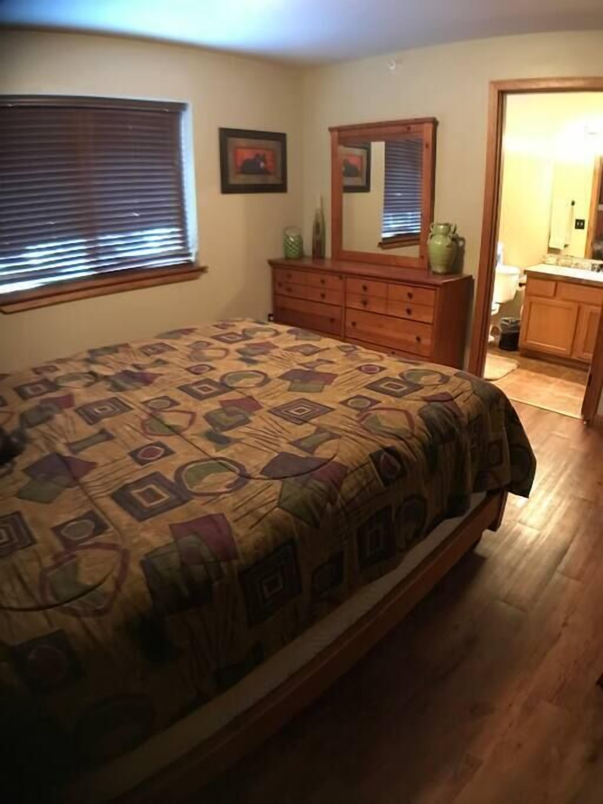 Una camera da letto con un letto, una cassettiera e un bagno visibile attraverso una porta aperta.