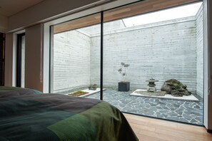 Habitació moderna amb un gran finestral corredís que dona a un pati interior. La llit té un edredó amb un disseny verd i negre.