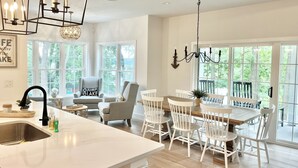 A spacious kitchen with a large island, white cabinetry, and a dining area with white chairs and a wooden table.