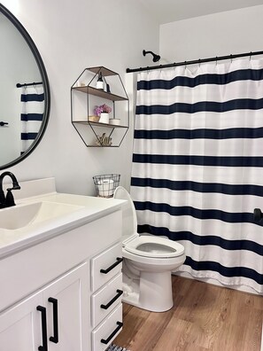 Une salle de bain avec un lavabo blanc, un robinet noir, des toilettes blanches et un rideau de douche à rayures noires et blanches.