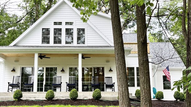 A white two-story house with a covered porch, multiple windows, and a flag.