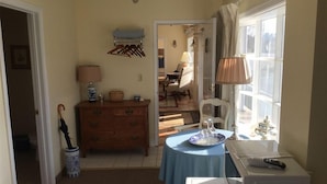 A compact room with a wooden dresser, a table with a blue tablecloth, a lamp, and a window with curtains. - The Beach Rose Inn (Wells)