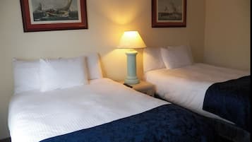 Een hotelkamer met twee bedden, een nachtkastje met een lamp en twee ingelijste foto's aan de muur.