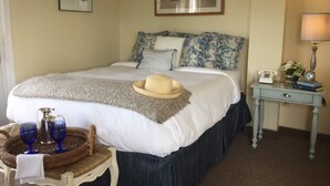 A neatly made bed with a white comforter, a beige hat, and two blue glass cups on a woven tray. - The Beach Rose Inn (Wells)
