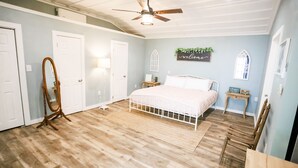 Une chambre à coucher avec un lit, un ventilateur de plafond, une chaise en bois et une petite table.
