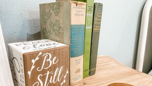 Un bloc de bois sur lequel est gravé le texte « I Be Still » et une pile de livres posée sur une surface en bois.