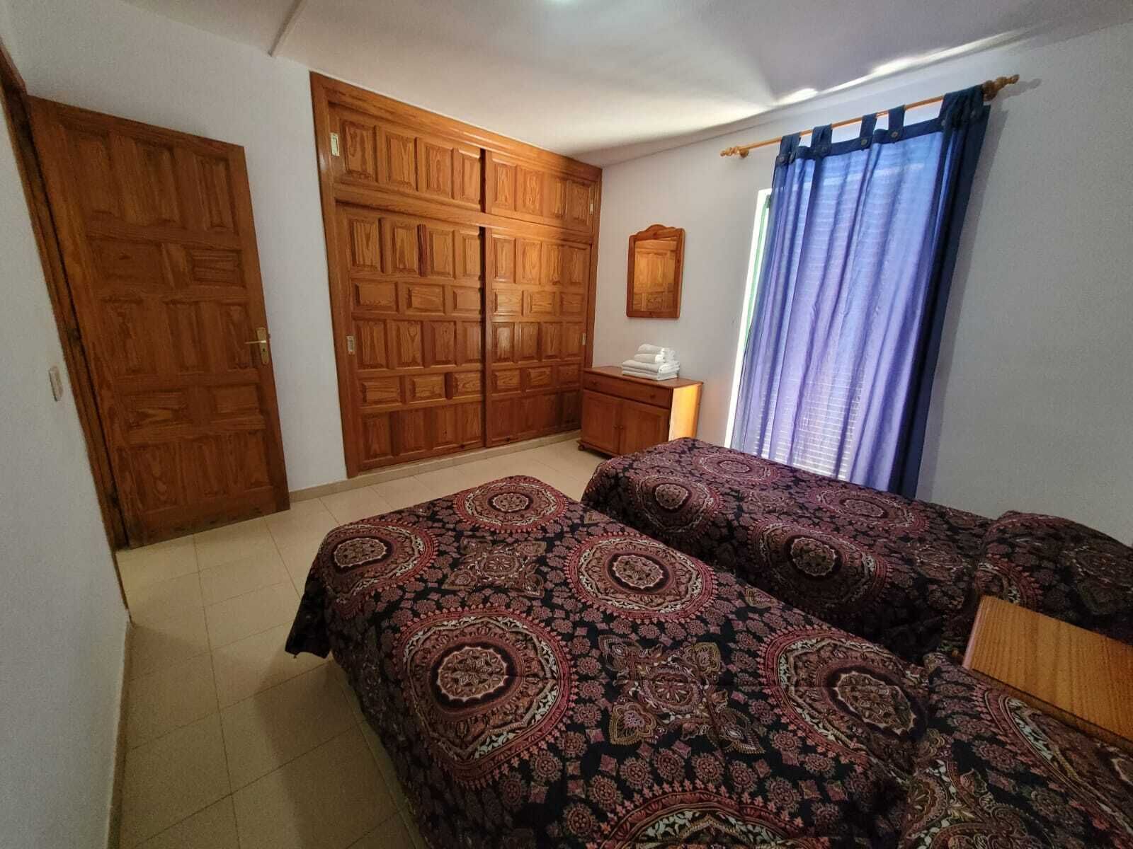 Ein Schlafzimmer mit zwei Betten, Holzschränken, einem kleinen Nachttisch und einem Fenster mit Vorhängen.