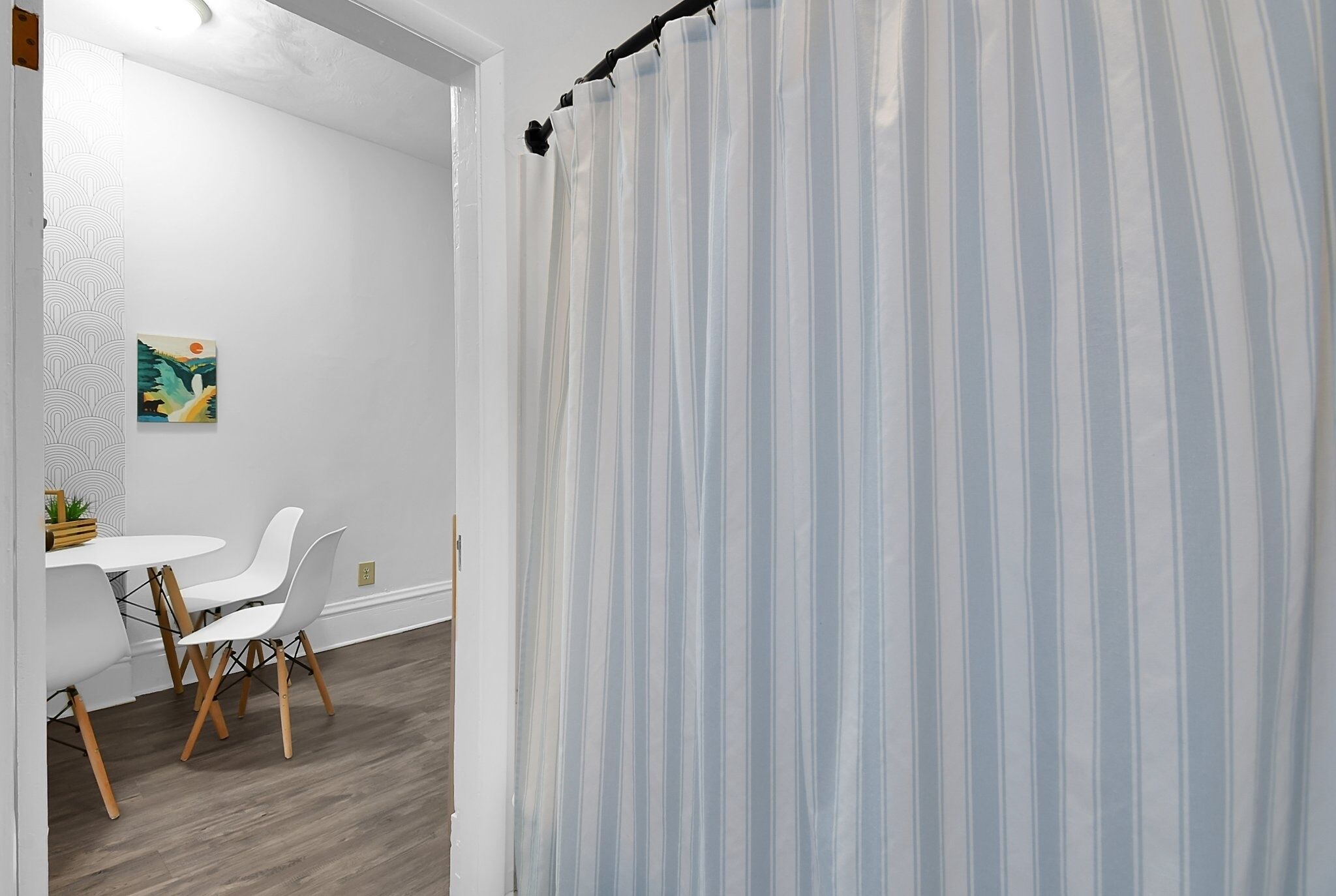 A room with a striped curtain, white walls, and a dining area with white chairs and a table.