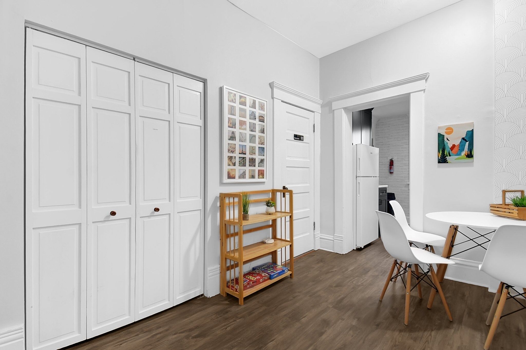 Una cocina moderna con armarios blancos, una estantería de madera y un comedor con sillas blancas y una mesa redonda.