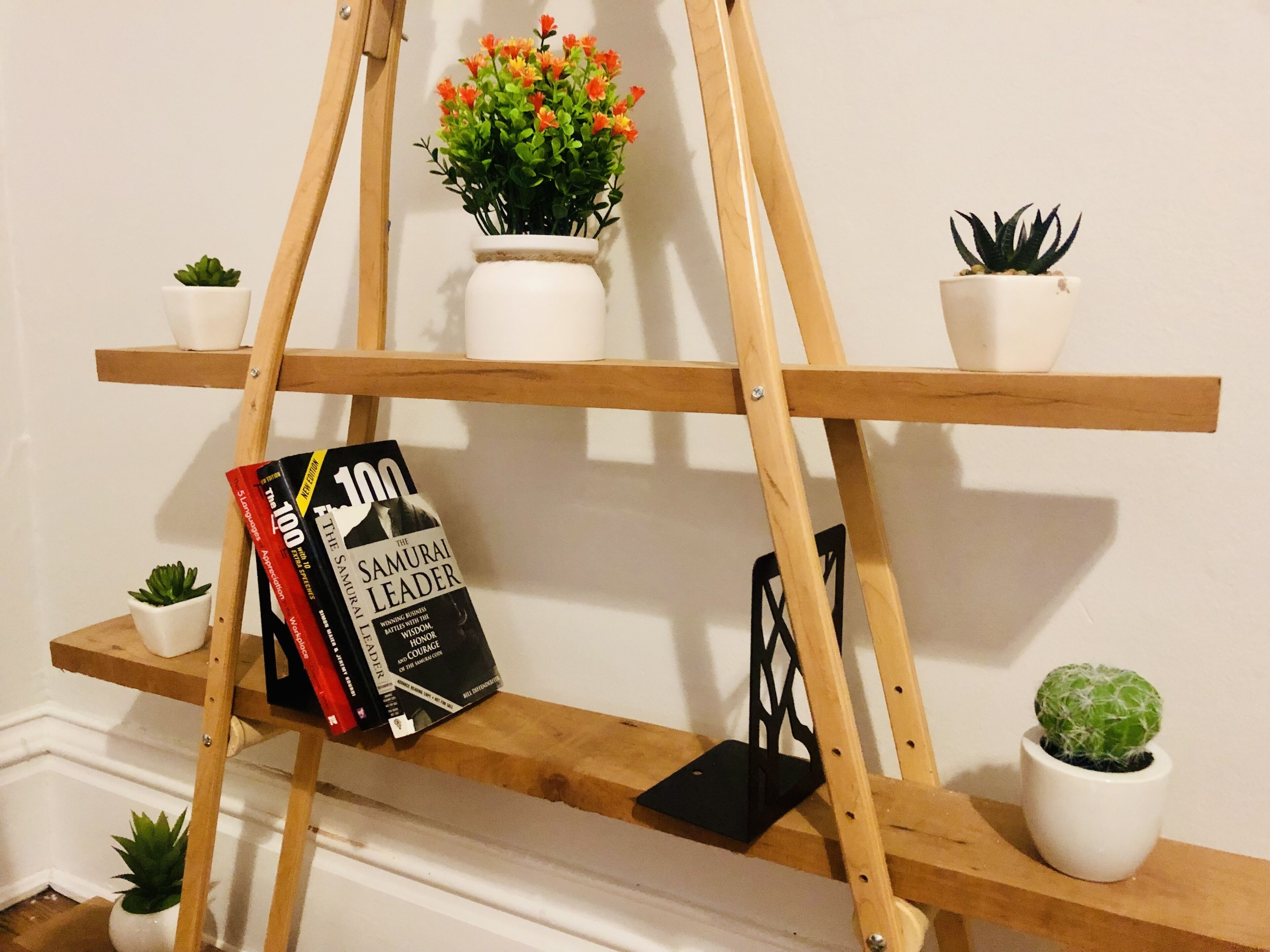 Een houten boekenkast met meerdere planken, waarop boeken, kleine potplanten en decoratieve objecten staan.
