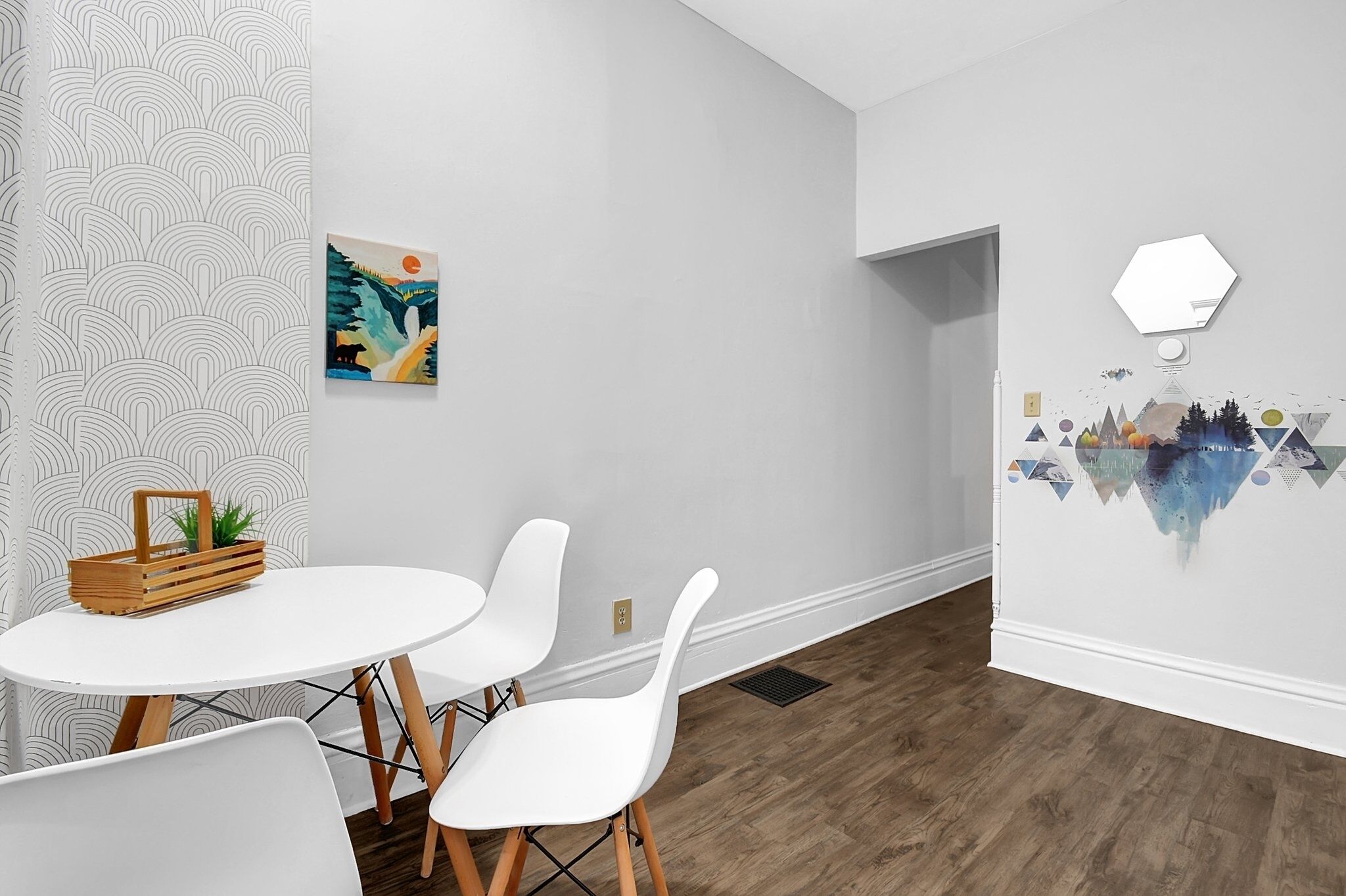 Ein modernes Zimmer mit rundem Tisch, weißen Stühlen, einer Wanddekoration und einem Wandpapier mit geometrischem Muster.