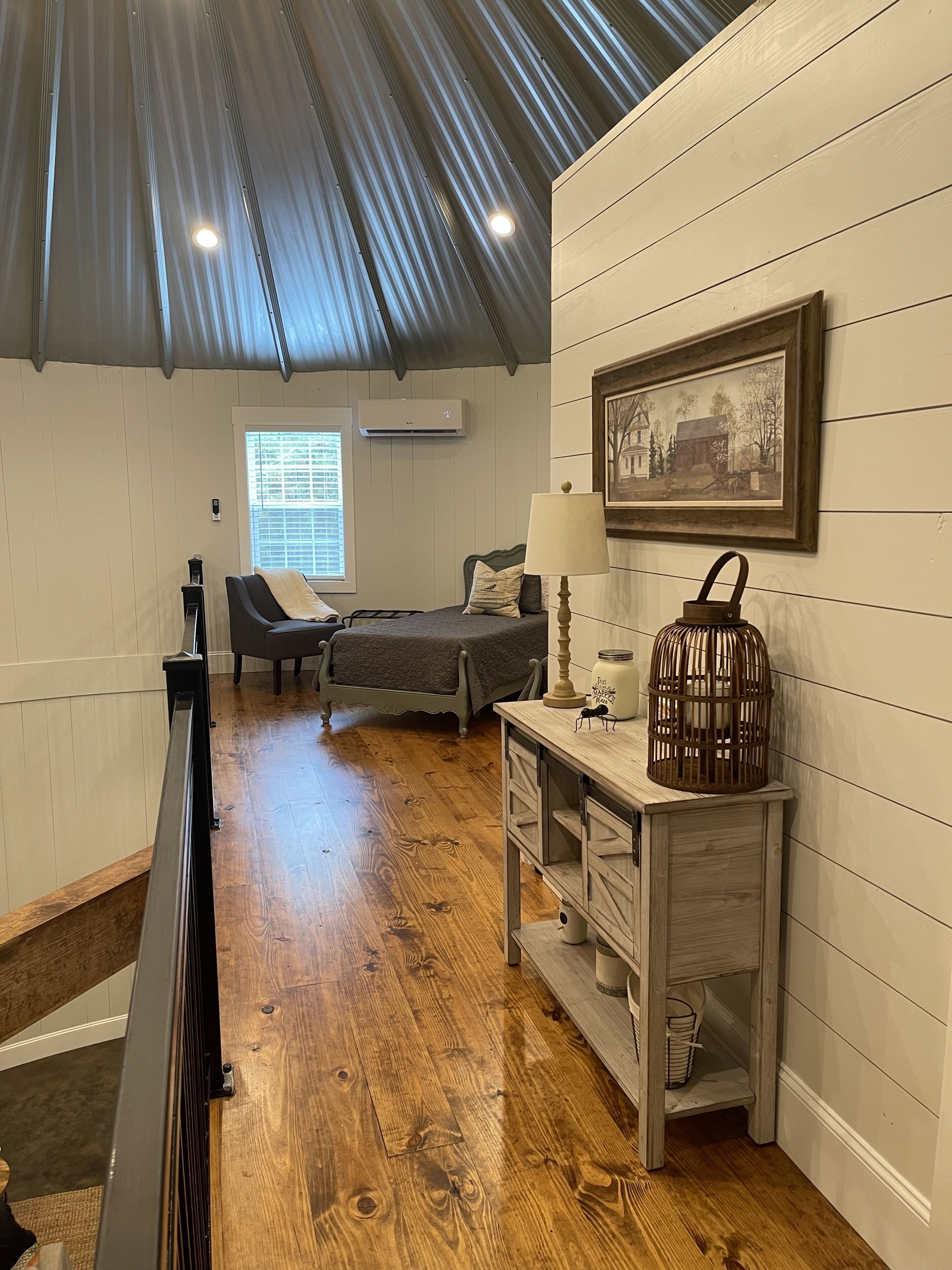 A cozy room with a bed, a chair, a desk, and a picture on the wall.