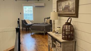 A cozy room with a bed, a chair, a desk, and a picture on the wall.