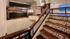 Un escalier en bois avec un palier carrelé, un luminaire suspendu et une vue sur la plage par une fenêtre.