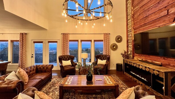 Un salon spacieux avec des canapés en cuir, une table basse en bois et un grand téléviseur. De nombreuses fenêtres offrent une vue sur l’extérieur.