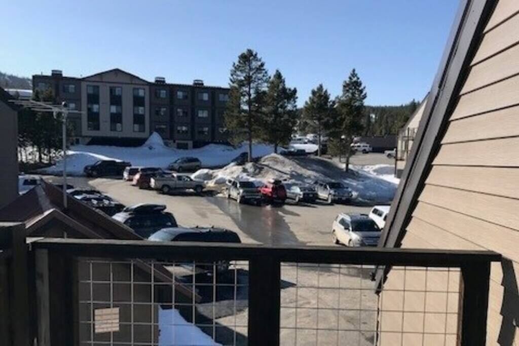 A parking lot with several cars and a snow-covered ground, surrounded by buildings.