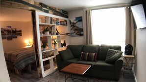 A cozy living room with a green sofa, a wooden coffee table, and a bookshelf filled with books and decorative items.