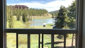 A view from a window overlooking a lake, surrounded by trees and a distant building.