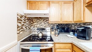 A compact kitchen with wooden cabinets, a stainless steel stove, a microwave, and a coffee maker.