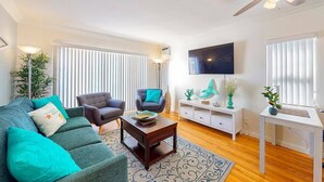 Un salon moderne comprenant un canapé, deux fauteuils, une table basse, un téléviseur et un bureau blanc.