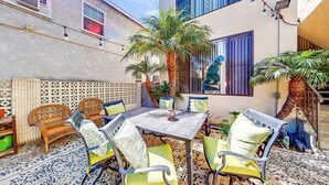 Une terrasse avec une table et des chaises, entourée de plantes en pot et d’un palmier.