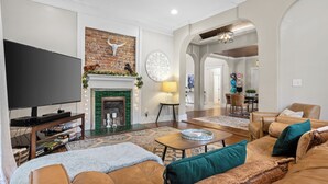 Una sala de estar con televisor, chimenea, sofá de cuero y un comedor al fondo.