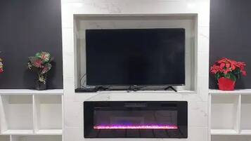 Ett modernt vardagsrum med en platt-TV som är monterad på en vit vägg, och som flankeras av två vita hyllor med krukväxter.