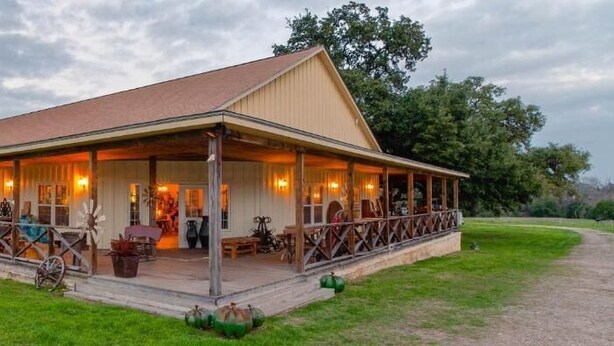 A large, single-story building with a covered porch and a dirt driveway. - Round Top Hotel (Round Top)