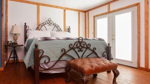 A bedroom with a wooden bed frame, a green bedspread, a brown upholstered bench, and a nightstand with a lamp. - Round Top Hotel (Round Top)