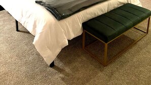 Un lit bien fait, avec une tête de lit noire, du linge de lit blanc et un banc vert.