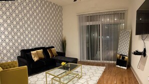 Un salon avec un canapé noir, un fauteuil jaune, une table basse en verre et un tapis blanc.