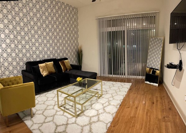 A living room with a black sofa, a yellow armchair, a glass coffee table, and a white rug.