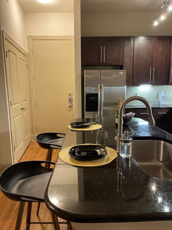 A modern kitchen with dark wooden cabinets, a stainless steel refrigerator, and a black granite countertop.