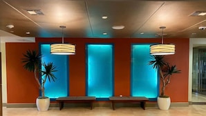 Un hall d’entrée avec un banc, deux plantes en pot et un mur orné de panneaux lumineux.