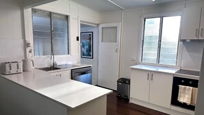 Une cuisine moderne avec des meubles blancs, un lave-vaisselle encastré, un évier en acier inoxydable et une fenêtre avec des stores.