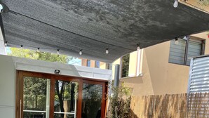 Une terrasse avec une table et des chaises, un barbecue et un espace couvert agrémenté de guirlandes lumineuses.