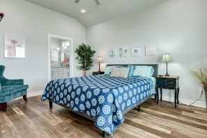Ein Schlafzimmer mit einem Bett, einem Sessel, einem Nachttisch, einer Lampe und einer Pflanze.
