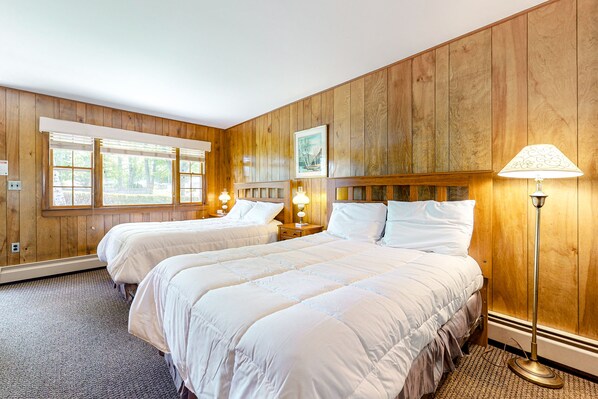 Una habitación con dos camas, paredes de paneles de madera, un ventanal grande y una lámpara de pie.