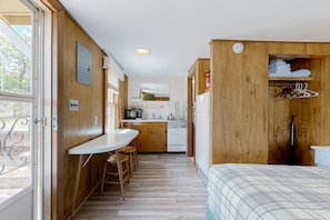 A compact kitchen with wooden cabinets, a white countertop, and a dining area with stools.