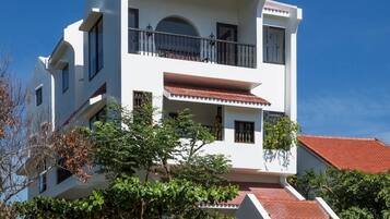 A multi-story white building with a red-tiled roof, balconies, and potted plants.