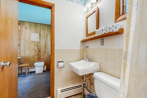 A bathroom with a wooden wall, a sink, a toilet, and a small stool.