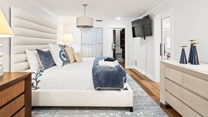 Een moderne slaapkamer met een groot bed, bedlampjes, een televisie en een garderobe.