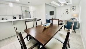 Una cocina moderna con armarios blancos, una mesa de comedor con sillas y una araña.