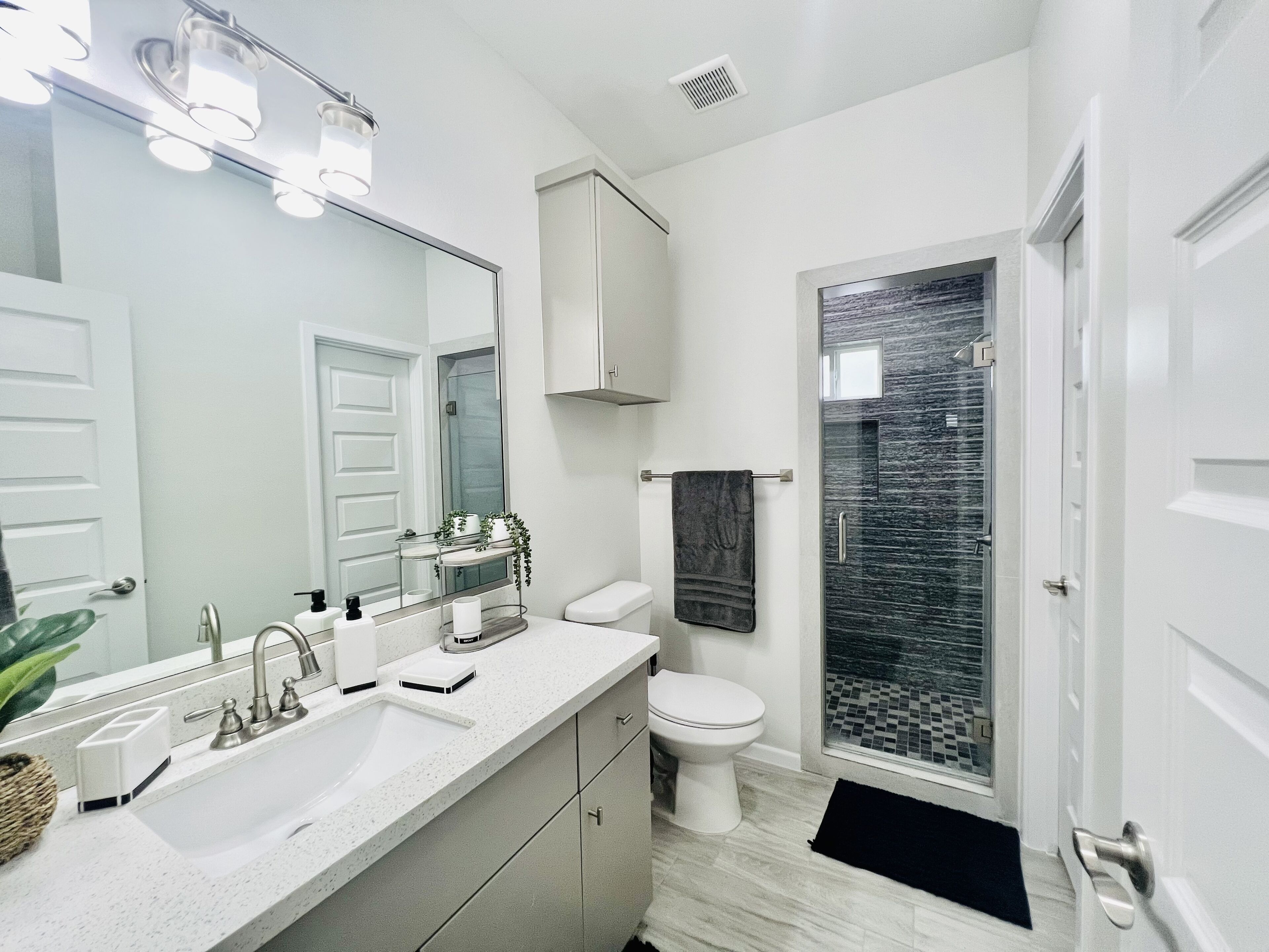 Un baño moderno con un espejo grande, un lavabo blanco, un inodoro y un box de ducha de vidrio.