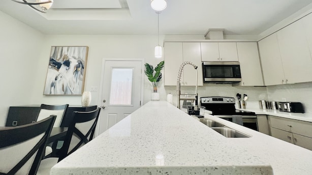 Una cocina moderna con una isla central, muebles blancos, electrodomésticos de acero inoxidable y un comedor con sillas y mesa.