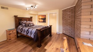 Une chambre avec un lit en bois, une table de chevet, un tableau et un mur en briques.