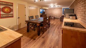 Une cuisine moderne avec un plancher en bois, un coin repas doté d’une grande table et de chaises, et un mur décoratif en briques.