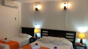 A hotel room with two single beds, each with an orange bedspread, white linens, and decorative flowers. There are bedside lamps and a wall-mounted air conditioner. - Oasis de Kiamu (Lifou)